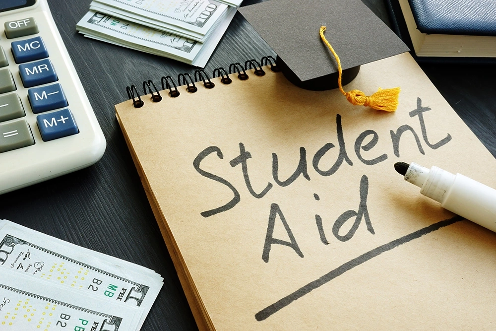 Student aid sign with a small black graduation cap and stack of dollar bills, symbolizing financial support and funding for education