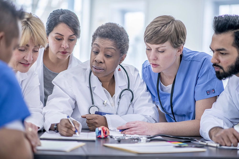 Senior medical professional guiding a group of diverse healthcare students in a clinical setting, providing hands-on mentorship and instruction