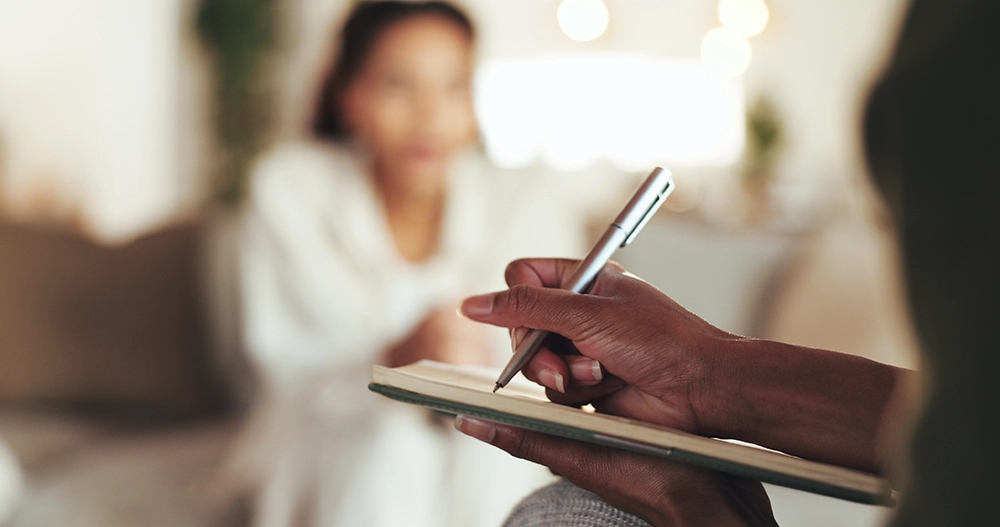Close-up of therapist’s hands holding clipboard and pen, taking notes during a counseling session with a patient, symbolizing mental health support